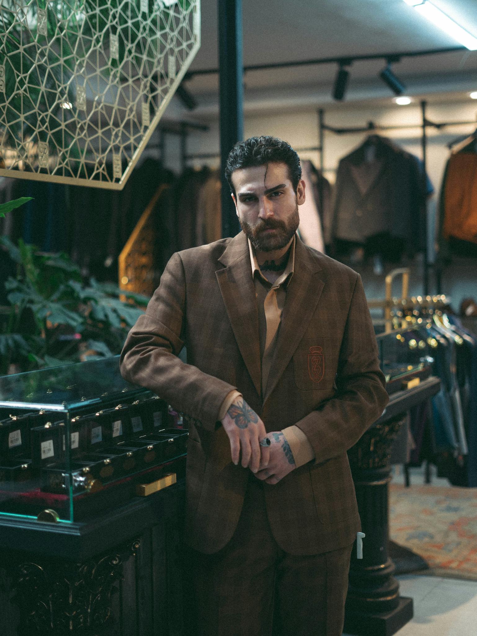 Man in a brown suit standing in a vintage clothing store with elegant decor.